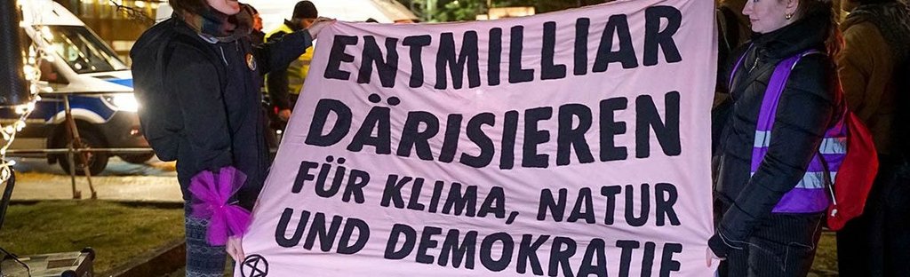 Protest im Januar 2025 gegen ein exklusives Lobby-Event des Axel­-Springer Verlags in Berlin. Transpi mit der Aufschrift: "Entmilliardärisieren. Für Klima, Natur und Demokratie."